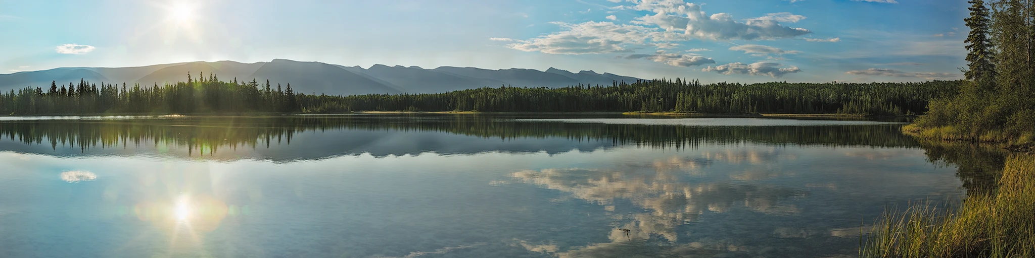 Sunrise over Boya Lake in northern British Columbia, Canada, with mountains and forest reflected in calm water
